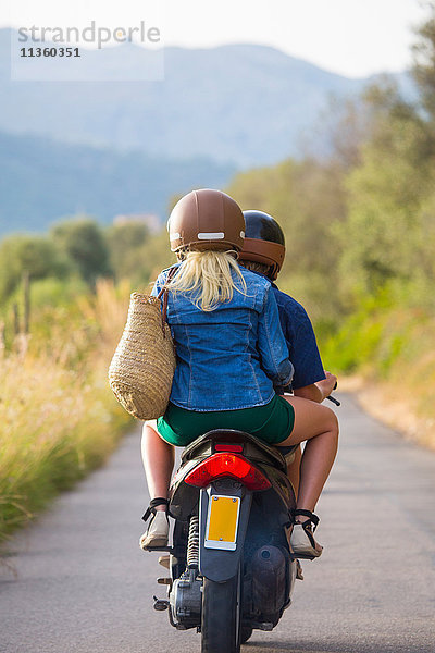 Rückansicht eines jungen Paares beim Mopedfahren auf einer Landstraße  Mallorca  Spanien