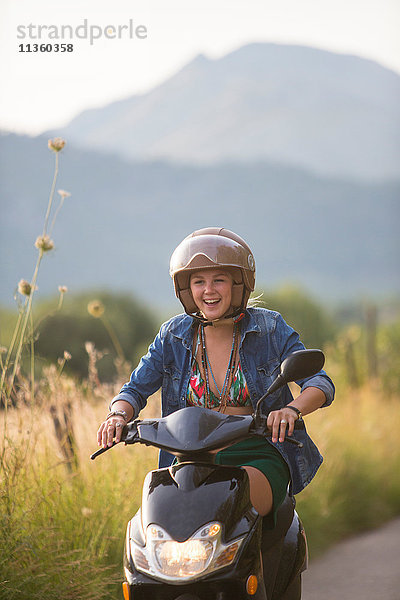 Glückliche junge Frau fährt Moped auf einer Landstraße  Mallorca  Spanien