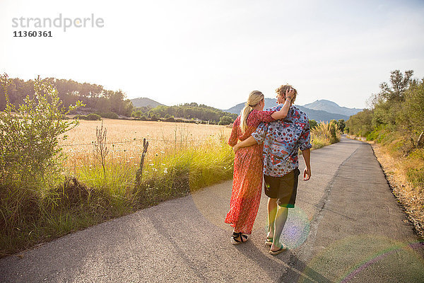 Rückansicht eines romantischen jungen Paares bei einem Spaziergang entlang einer Landstraße  Mallorca  Spanien