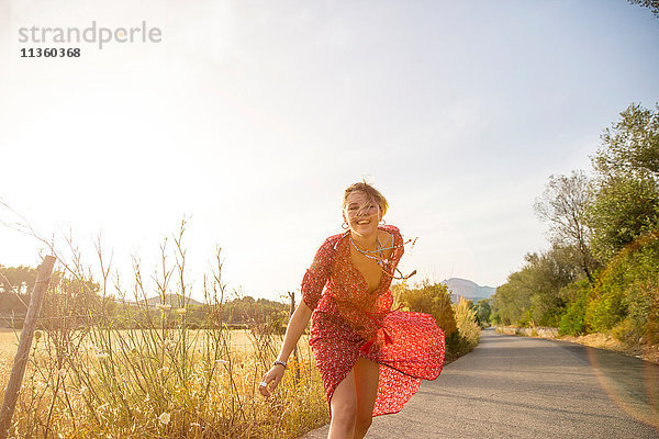 Glückliche junge Frau in rotem Kleid läuft auf Landstraße  Mallorca  Spanien
