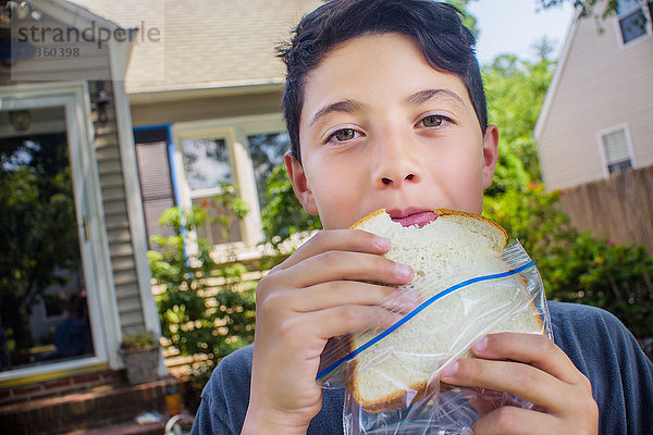Porträt eines süßen Jungen  der im Garten ein Sandwich isst