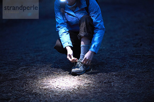 Wanderin mit Stirnlampe beim nächtlichen Schnürsenkelbinden von Wanderschuhen