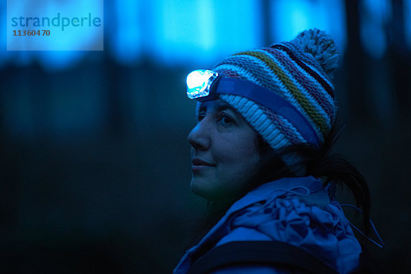 Weibliche Wanderin mit Stirnlampe  die nachts aus dem Wald über ihre Schulter schaut