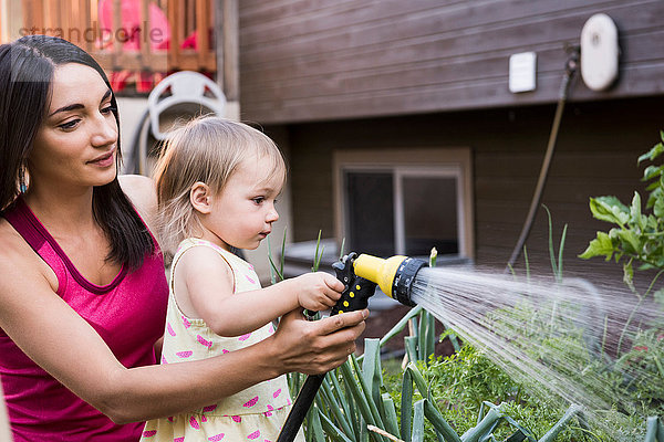 Mutter und Tochter im Garten  gießen die Pflanzen zusammen mit dem Schlauch