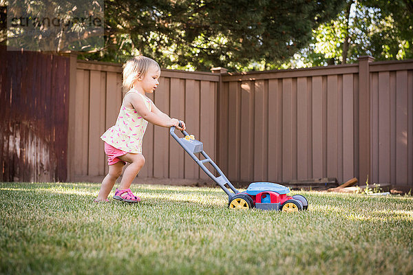 Junges Mädchen im Garten  schiebt Spielzeug-Rasenmäher