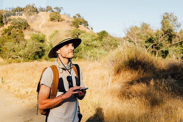 Wanderer hält Smartphone in der Hand und schaut weg  Malibu Canyon  Kalifornien  USA