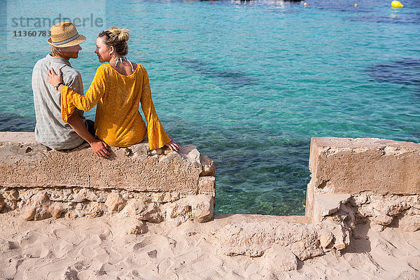 Rückansicht eines auf einer Mauer am Meer sitzenden Paares  Mallorca  Spanien