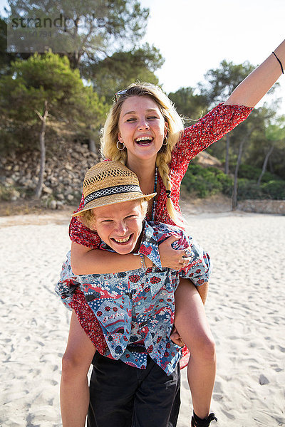 Mann am Strand gibt lächelnder Frau Huckepack  Mallorca  Spanien