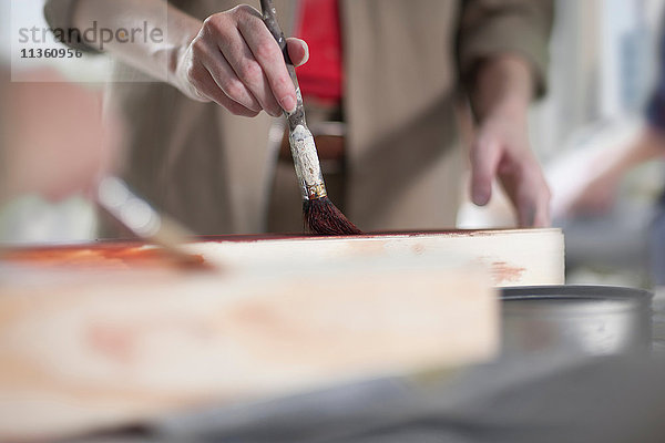 Schnappschuss einer Tischlerin beim Bemalen von Holzbeize in einer Möbelwerkstatt