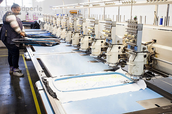 Fabrikarbeiterin  die in einer Bekleidungsfabrik Stoff für eine programmierte Schnellnähstickmaschine vorbereitet
