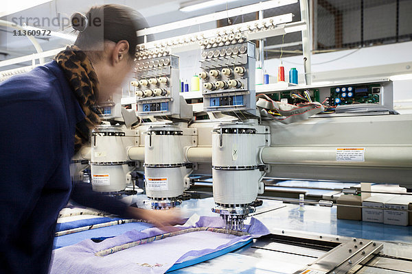 Fabrikarbeiterin  die in einer Bekleidungsfabrik Stoff für eine programmierte Schnellnähstickmaschine vorbereitet