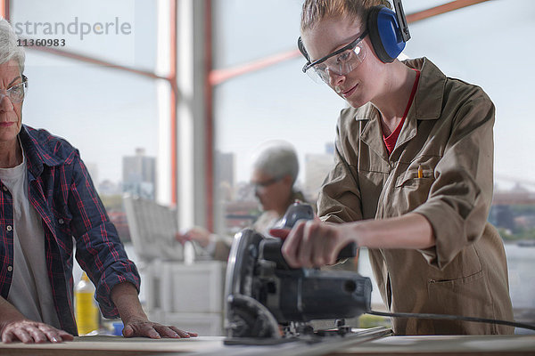 Tischlerlehrling lernt den Umgang mit der Motorsäge in einer Möbelwerkstatt