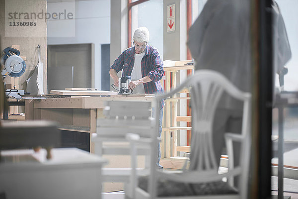 Tischlerin mit Schleifmaschine in Möbelbauwerkstatt