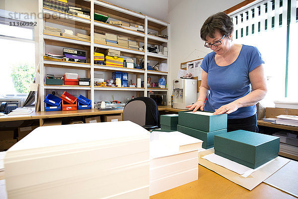Arbeitnehmerin packt Auftrag in Pappkarton in Druckereiwerkstatt