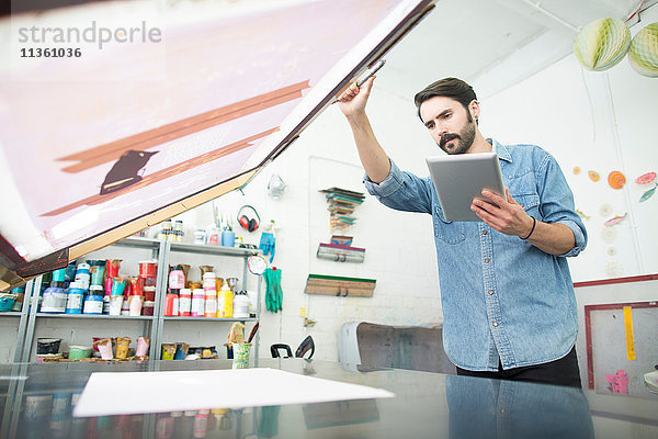 Männlicher Drucker bereitet Papier und Siebdruck im Druckmaschinenstudio vor