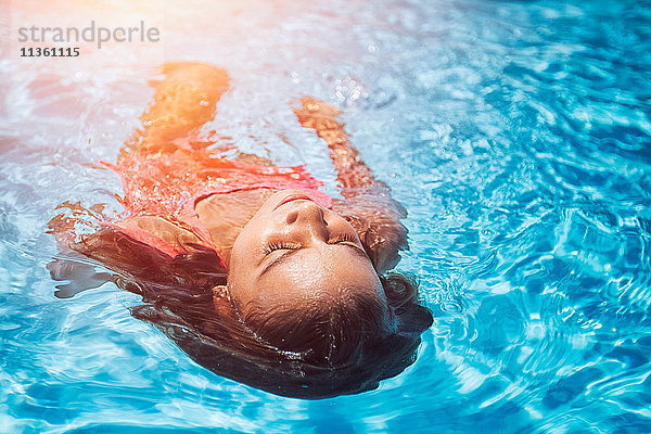 Mädchen schwebt auf dem Rücken im sonnenbeschienenen Swimmingpool