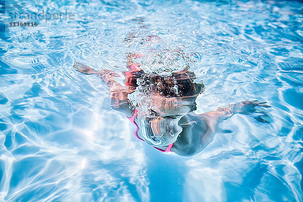 Mädchen schwimmt unter Wasser im sonnenbeschienenen Schwimmbad