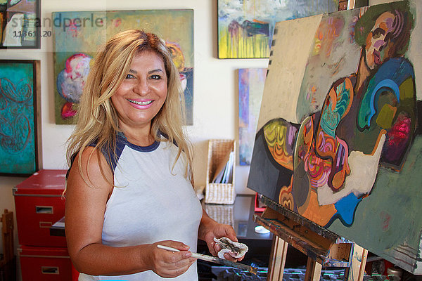 Künstler malt Kunstwerke auf Leinwand  schaut lächelnd in die Kamera