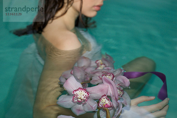 Schnappschuss einer jungen Frau im Schwimmbad des Kurortes mit einem Strauss violetter Orchideen