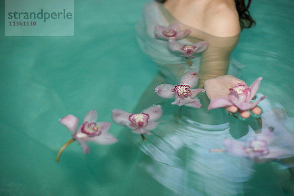 Schnappschuss einer jungen Frau im Schwimmbad eines Heilbades mit schwimmenden violetten Orchideen