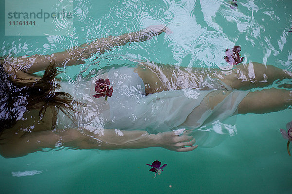 Blick von unten auf eine Frau  die mit Orchideen unter Wasser im Schwimmbad des Heilbades schwimmt