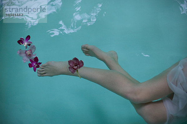 Nackte Beine und Füße einer Frau  die mit Orchideen unter Wasser im Whirlpool schwimmt