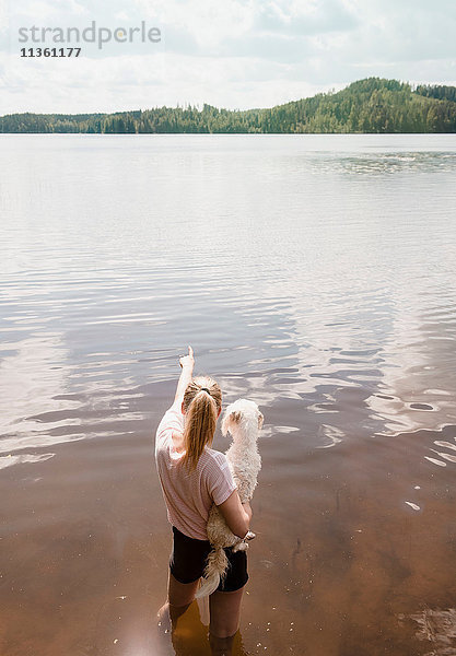 Frau steht im See und trägt einen Hund mit Coton de Tulear  Orivesi  Finnland