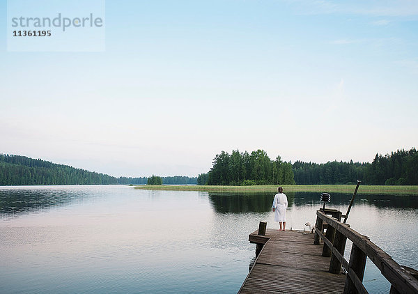 Frau im Bademantel mit Hund coton de tulear  der vom Seepier aus schaut  Orivesi  Finnland