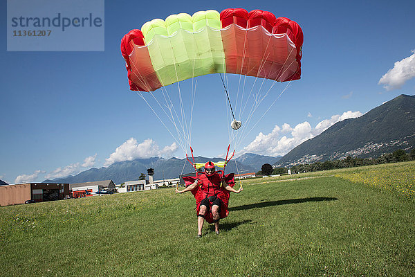 Fallschirmspringer landet Fallschirm auf dem Feld. Steuerung und Verlangsamung seines Fallschirms durch Ziehen der Bremsknebel  Locarno  Tessin  Schweiz