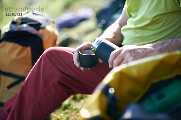 Schrägansicht eines Wanderers  der Tee aus der Flasche gießt