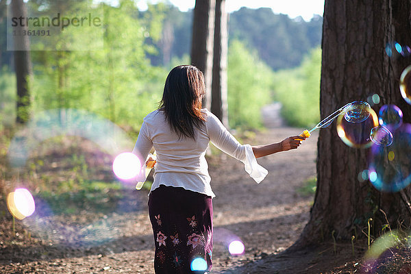 Rückansicht einer Frau im Wald beim Blasenmachen mit dem Blasenzauberstab
