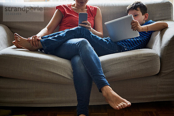 Mutter und Sohn entspannen sich auf dem Sofa mit digitalem Tablet und Smartphone