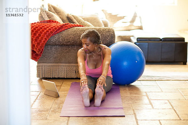 Frau auf Yogamatte mit digitalem Tablett  Stretching