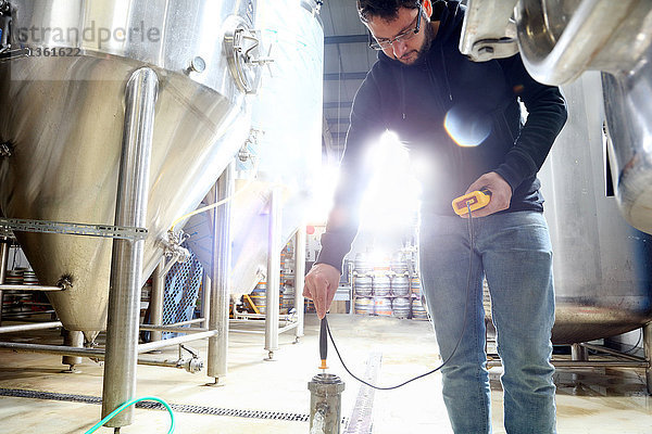 Arbeiter in einer Brauerei  der die Wassertemperatur im Brautank überprüft