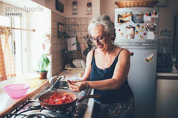 Frau schneidet lächelnd Tomaten in Kochtopf