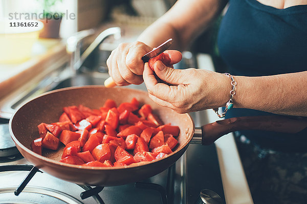 Schrägansicht einer Frau  die Tomaten in einen Kochtopf schneidet