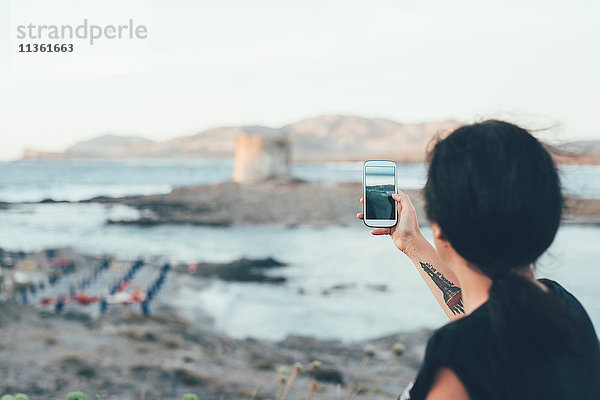 Rückansicht einer Frau  die mit ihrem Smartphone den Strand fotografiert  Stintino  Sassari  Italien