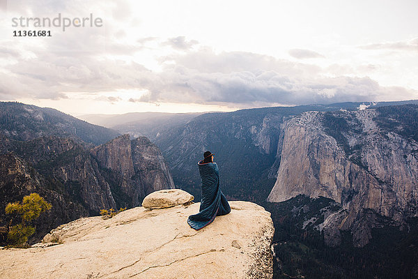 Junge Frau in eine Decke gehüllt  auf dem Gipfel eines Berges stehend  mit Blick auf den Yosemite National Park  Kalifornien  USA
