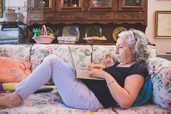 Frau liegt mit Laptop auf dem Sofa