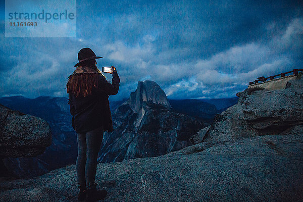 Junge Frau fotografiert in der Abenddämmerung auf einem Felsen mit Blick auf den Yosemite-Nationalpark  Kalifornien  USA