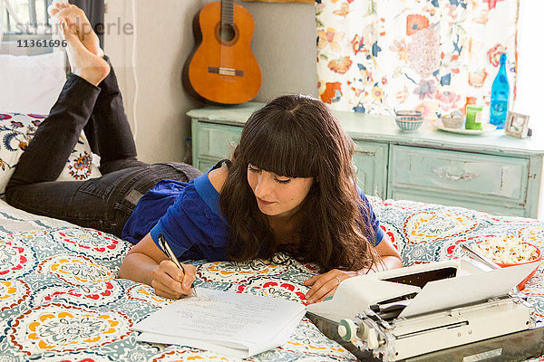 Junge Frau auf dem Bett liegend  Schreibmaschine benutzend  Notizen schreibend
