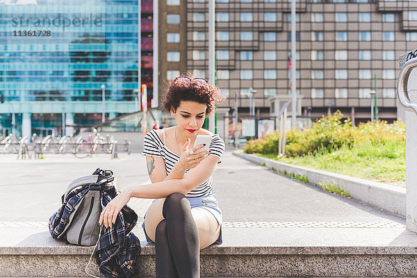Frau im Stadtgebiet sitzend  SMS auf Smartphone  Mailand  Italien