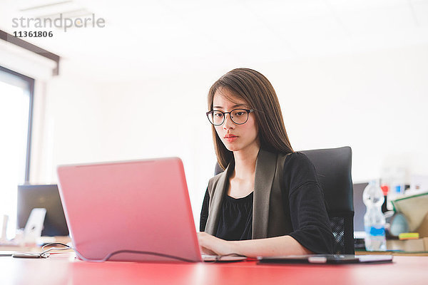 Junge Frau am Büroschreibtisch beim Tippen am Laptop