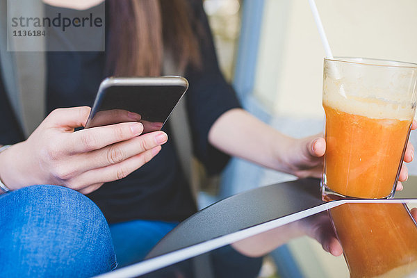 Geschnittene Aufnahme einer jungen Frau mit einem Smartphone im Straßencafé