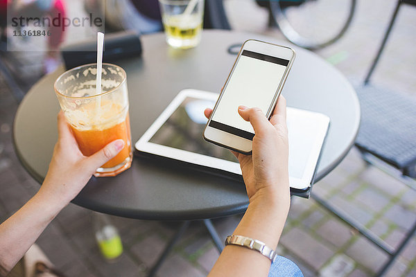 Abgetrennte Aufnahme der Hände einer jungen Frau mit einem Smartphone im Straßencafé