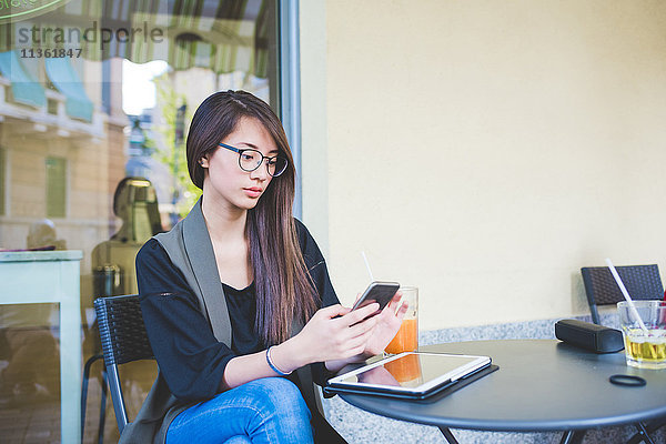 Junge Frau liest im Straßencafé Smartphone-Texte