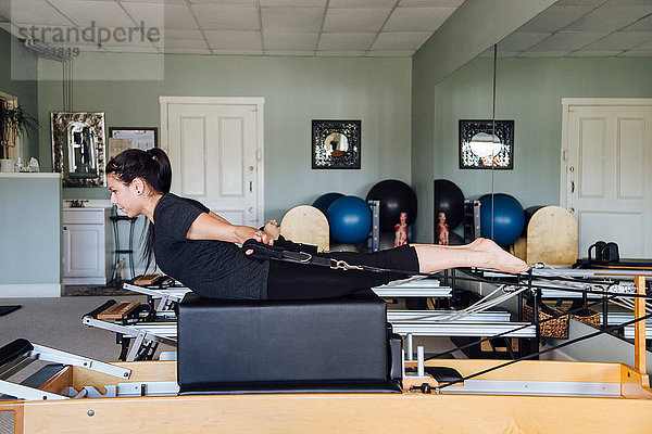 Seitenansicht einer Frau im Fitnessstudio mit Pilates-Reformer
