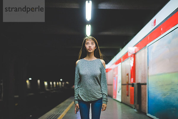 Porträt einer jungen Frau  die nachts auf dem Bahnsteig steht und auf den Bahnsteig starrt