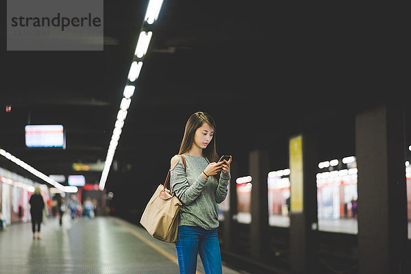 Junge Frau mit Smartphone auf dem Bahnsteig bei Nacht