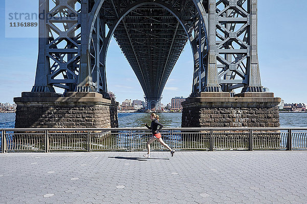 Junge Frau  die im Freien trainiert und unter der Williamsburg Bridge läuft  New York City  USA